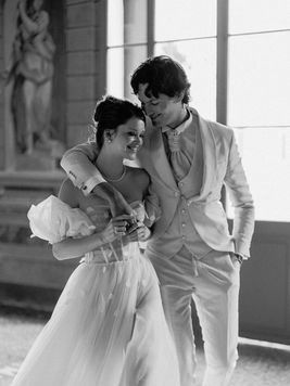 schwarzweiss Foto von verliebtem Brautpaar geht Arm in Arm und schaut sich tief in die Augen. Sie sind im grossen Galerieraum der Villa Mosconi Bertani in Italien