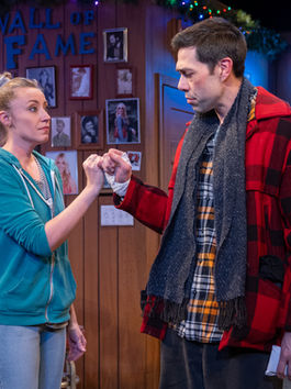 In a bar, a man and woman are locked in a pinky promise, each with a serious expression.