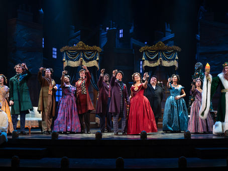 A company of actors in Victorian-era costumes raise a glass.