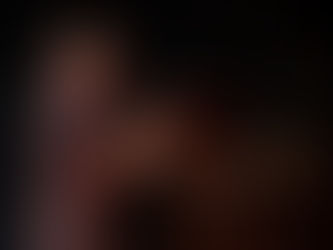 A person in a dress stands next to a dresser, upon which are miniature furniture items