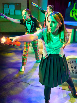 Three women in modern clothes stand in tense poses with flashlights pointing out