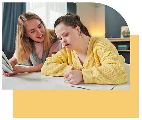 Image of a person with Downs Syndrome writing with a person next to them with a yellow box underlay behind it.