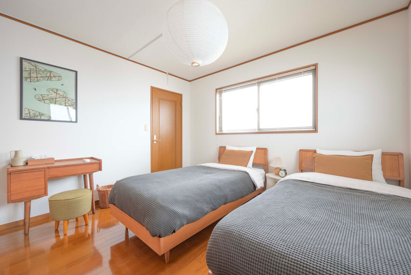 Bedroom 3 with two single beds, walk-in closet, wood-toned dresser with mirror, and stool in a white-walled room with wood flooring
