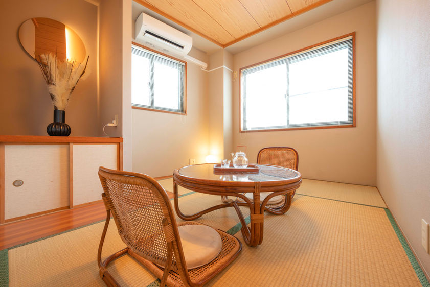Japanese tatami room with rattan low table, rattan floor chairs, display shelf, and air conditioning in a Japanese guesthouse