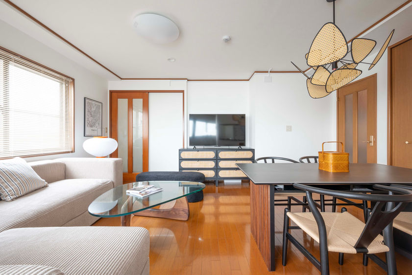 Living and dining area with 55-inch TV, 6-seat dining table, fabric sofa, white walls, and wood flooring in a Japanese guesthouse