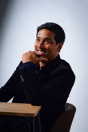 Male consultant in navy jacket seated on grey backdrop at LPS Headshot Studio during company profile photo session