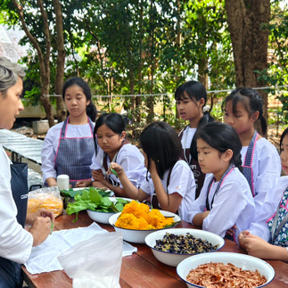 Gigi Payne guiding young student through leaf selection during eco-print craft session at Wat Sukato monastery Thailand