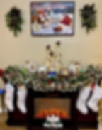 Festive mantle with garland, white stockings, and Christmas village decor. A painting of a snowy scene hangs above; warm, cozy ambiance.