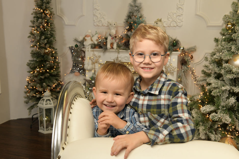 Zwei lächelnde Brüder vor beleuchteten Weihnachtsbäumen im Fotostudio in Wiener Neustadt