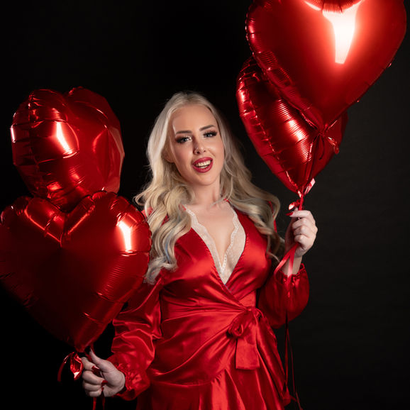 Blonde Frau in rotem Outfit mit Herzballons bei einem kreativen Portraitshooting in Wiener Neustadt