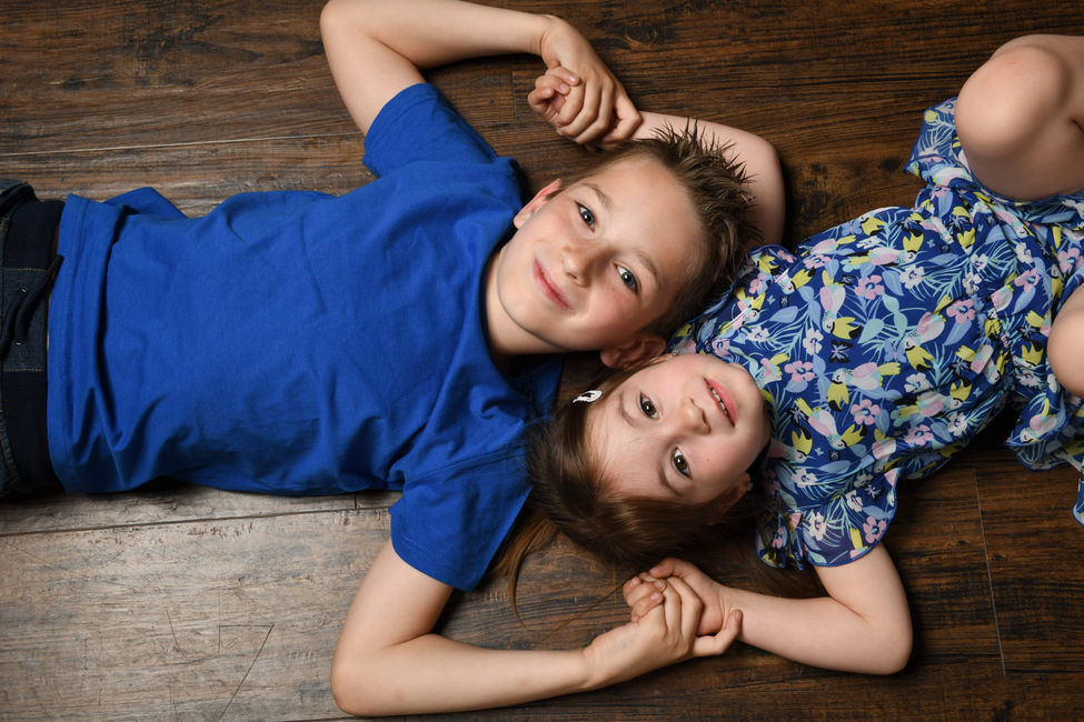 Junge und Mädchen liegen lächelnd auf einem Holzboden beim Geschwister-Fotoshooting in Wiener Neustadt