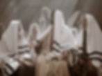 Men in robes sit in a dim room with soft light, engaged in deep discussion. The mood is solemn and contemplative.
