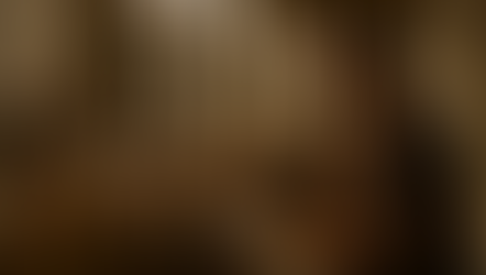 Man in brown robe reading scroll to attentive crowd in ancient, columned building. Warm lighting, serious expressions, historical setting.