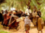 A man rides a donkey surrounded by people waving palm branches, wearing robes, in a forest setting. The mood is joyful and lively.