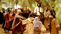 People cheer and wave palm branches at a man on a donkey in a lush setting. Earthy tones dominate. Joyful mood.