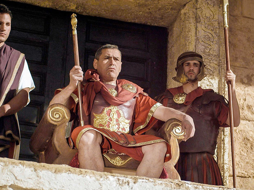 Roman commander in red and gold armor sits authoritatively on a throne, flanked by guards in a stone setting. Stoic mood, no text visible.