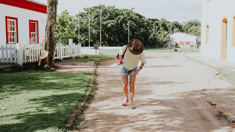A woman in casual attire walks down a sunny street in Porto Seguro, Bahia, Brazil.