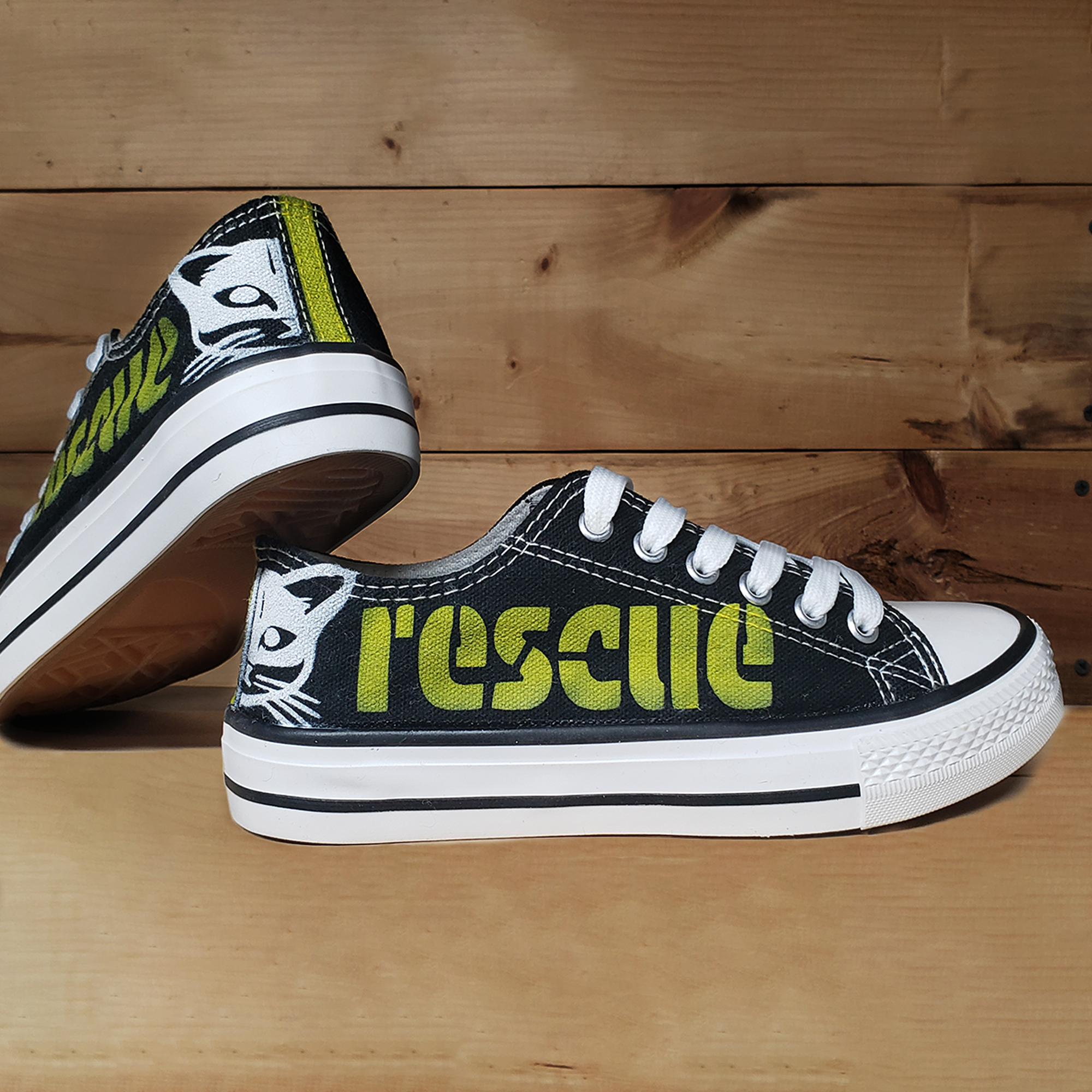 Black canvas low top sneakers with a greenish-yellow rescue on the side and half a cat face on the back