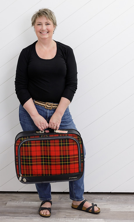 woman in black shirt and jeans short blonde hair holding a plaid patterned suitcase