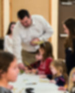 A man helps children with crafts at a table.