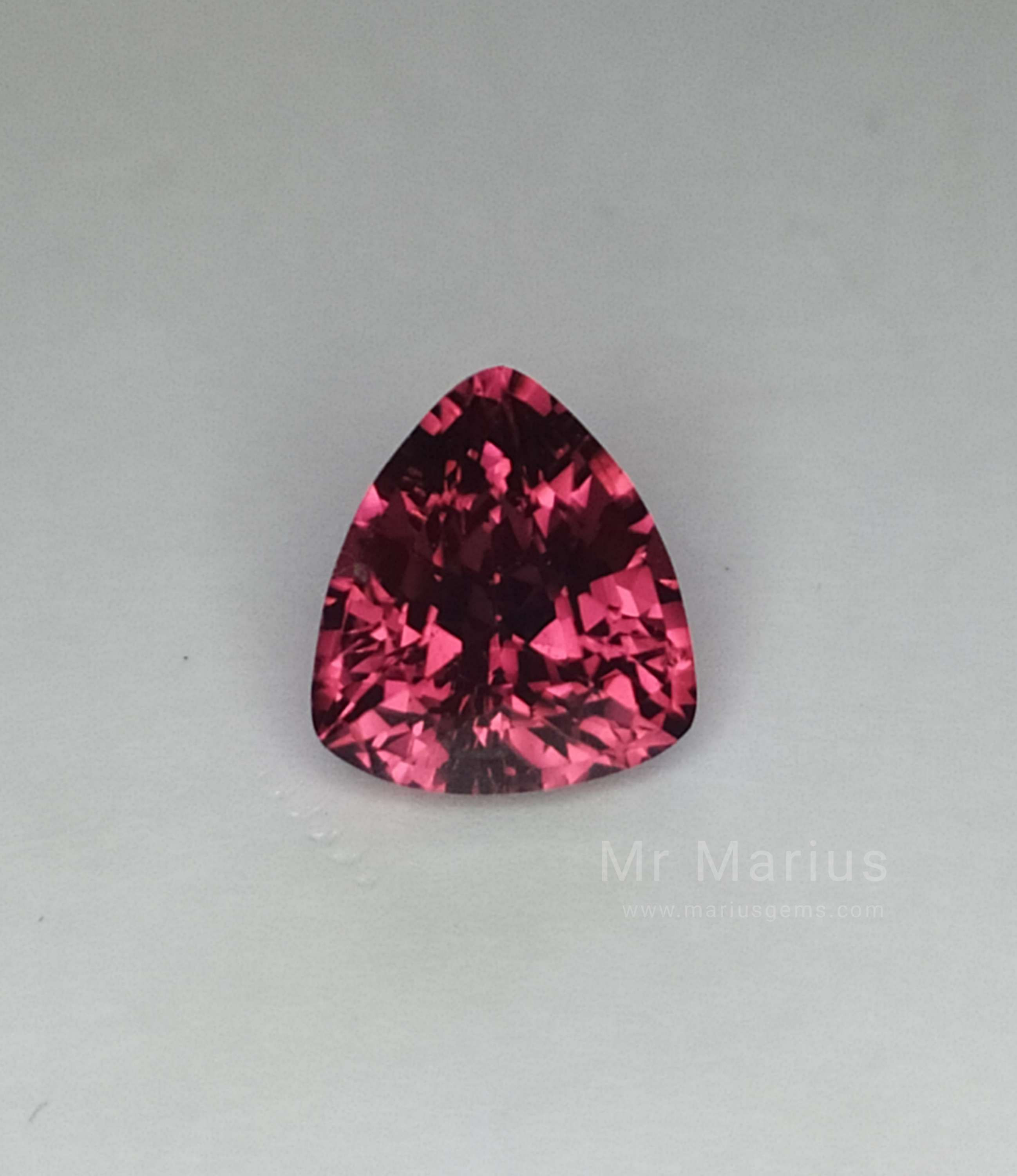 Triangular cut rhodolite garnet, bright reddish pink.