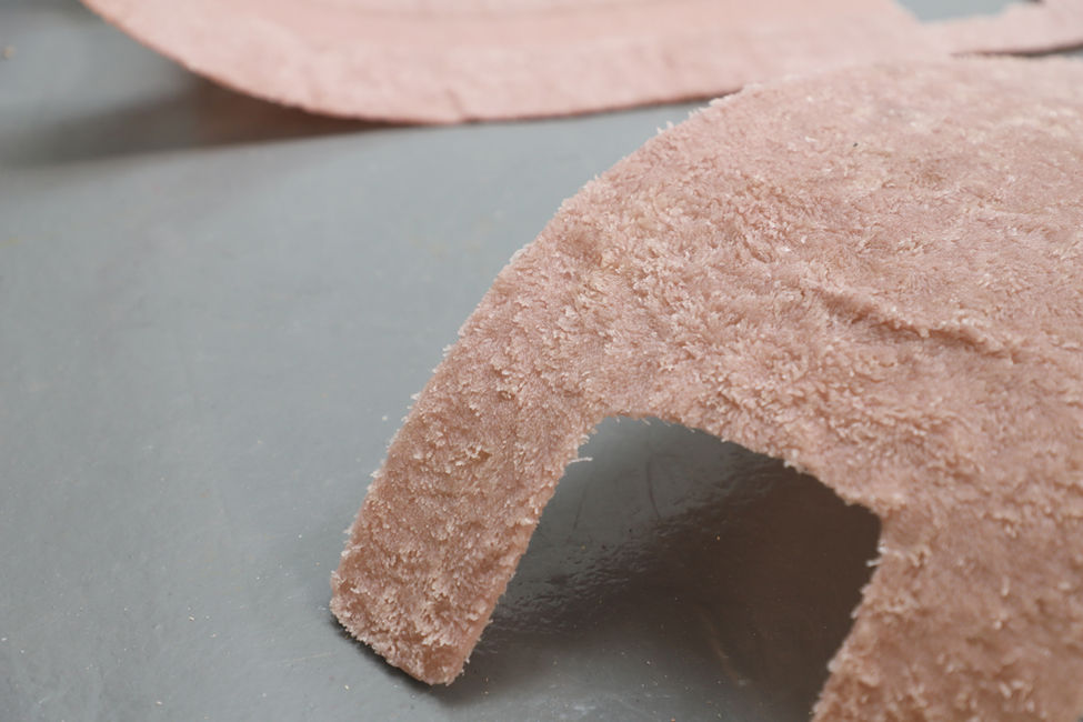 Detail of sculpture made of stiffened pale pink bath towel on gray wooden floor. Lola Carlander Wade.