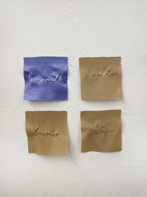 Sculpture. Four fabric squares with hand-sewn cursive words in hair and floss: "buy milk", "I was here", "breathe", "call mom". Lola Carlander Wade.