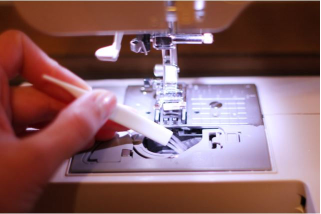 Close-up view of sewing machine bobbin area with lint buildup