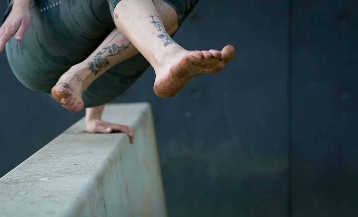 The feet and lower body of a person vaulting over a concrete obstacle.