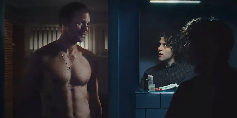 Shirtless man stands in dimly lit room; two people visible in bathroom mirror with toiletries around. Mysterious and tense mood.