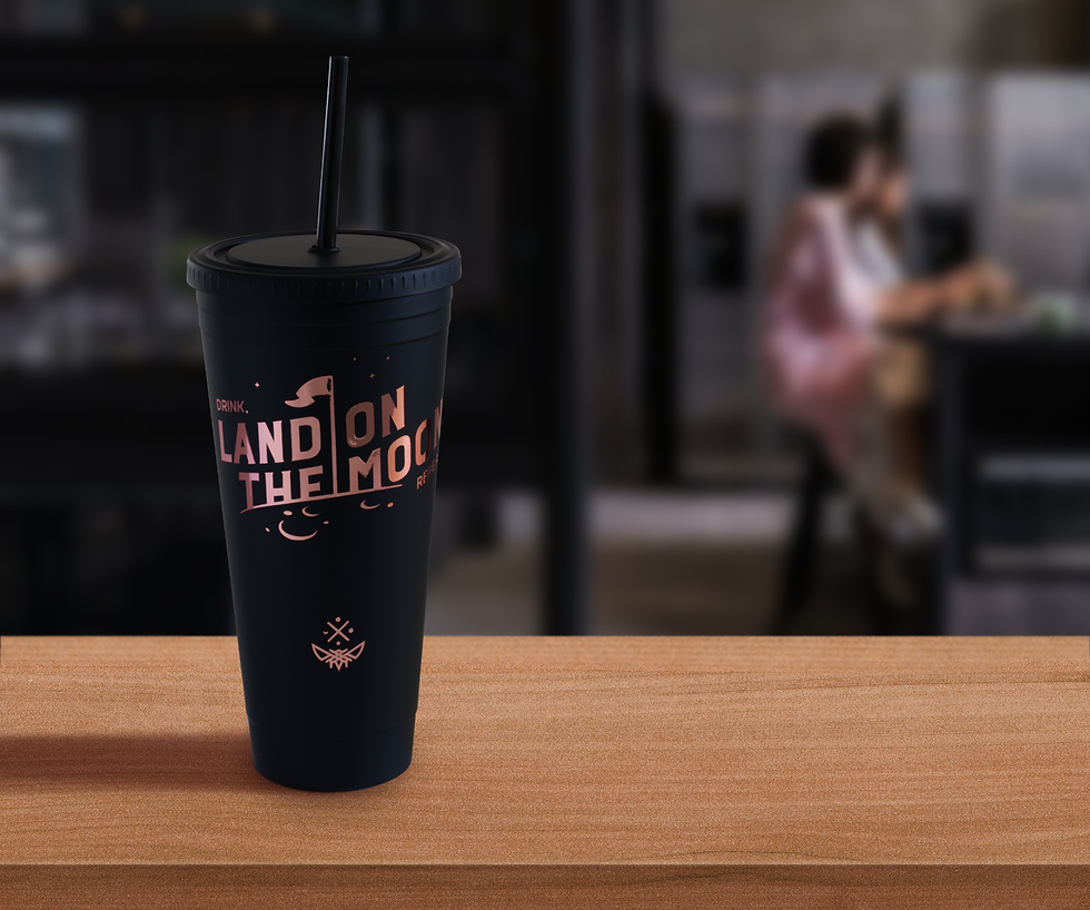 A black cup with a straw on a table with words saying: Drink, land on the moon, repeat.