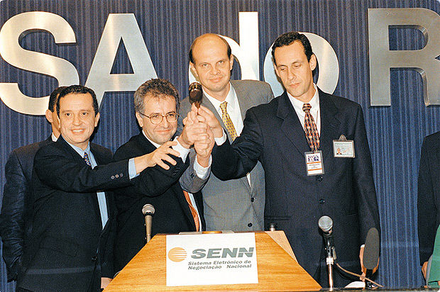 Quatro homens de terno, segurando um martelo de madeira juntos.