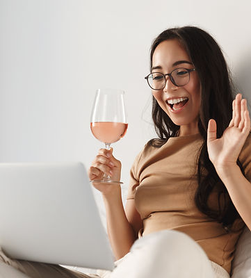 Image of young happy asian woman having video call, sitting on bed and drinking wine while