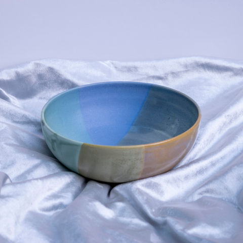 Handmade ceramic bowl with blue and gold glaze set on a silver cloth.