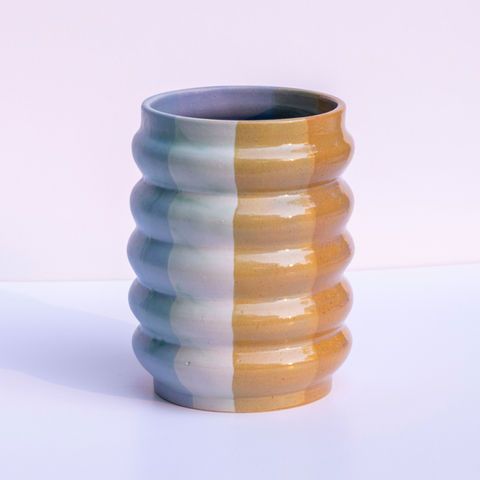 Colorful ceramic vase with blue, white and yellow stripes on white background.