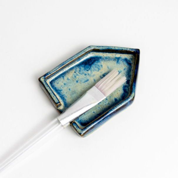 Blue ceramic art palette and brush, studio shot against a white backdrop