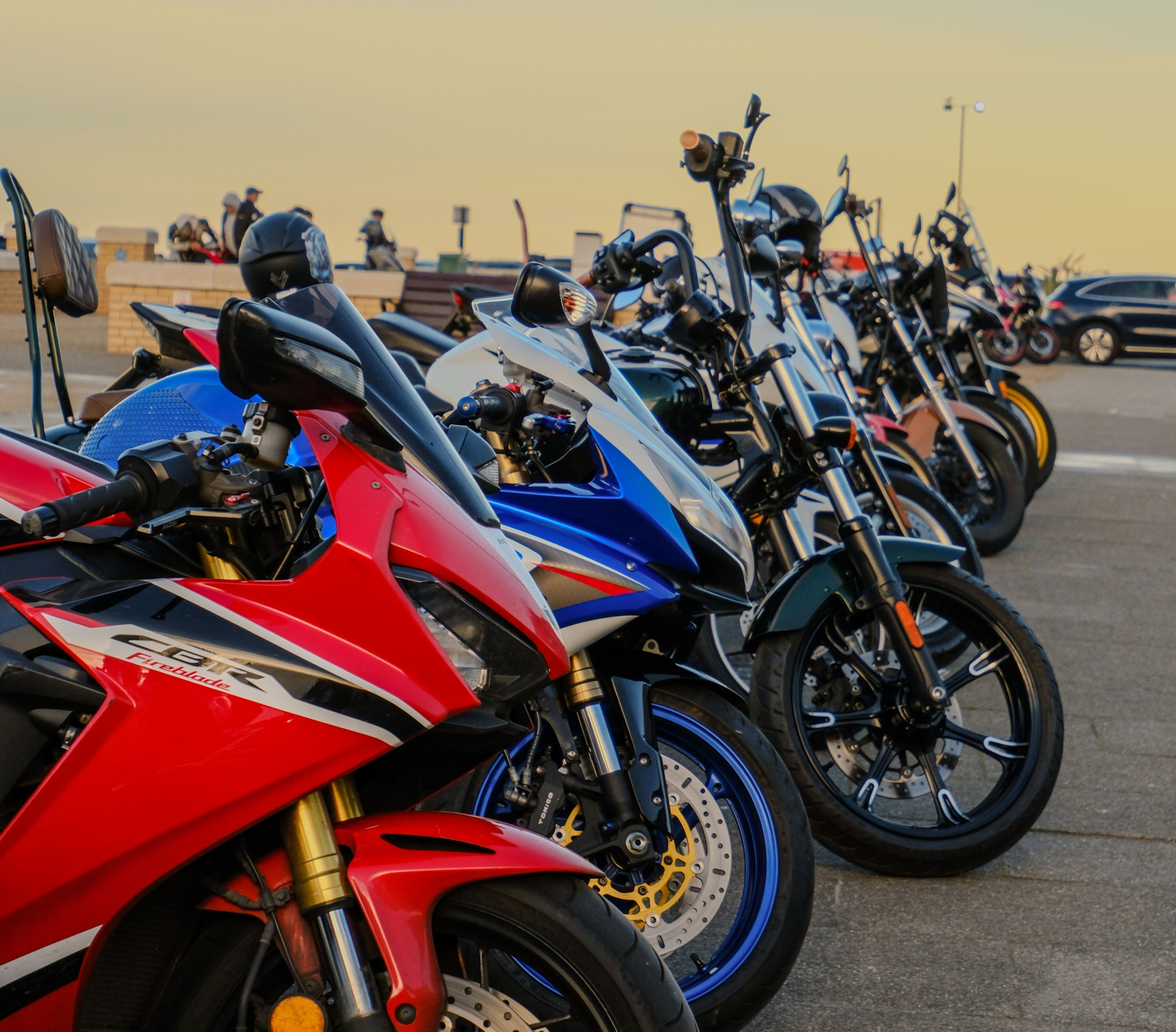 A line of sportbikes and cruisers parked along a coastal lot at sunset near the beach.