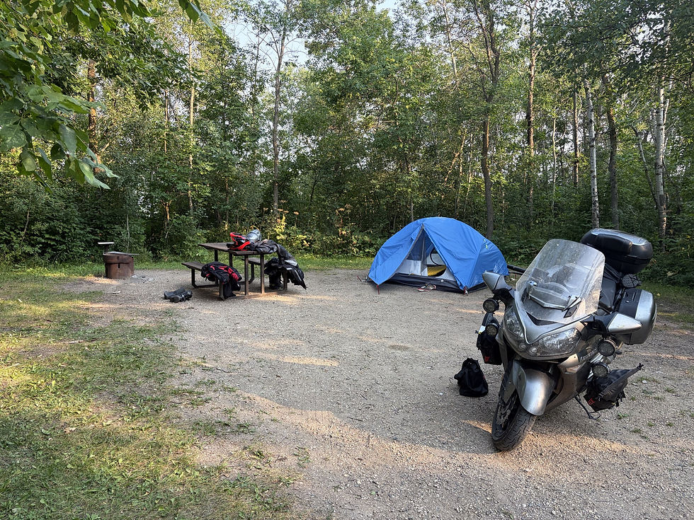A blue tent, picnic table covered in riding gear, and the Kawasaki Concours at a wooded campsite.