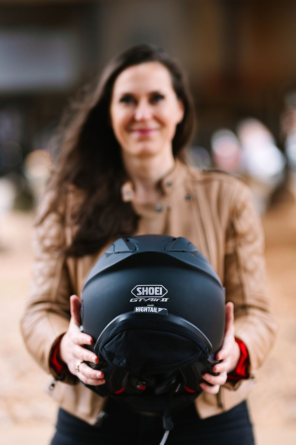 Jen holding out a matte black Shoei GT-Air II helmet fitted with a Hightail hair protector.