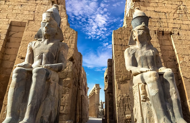Massive seated statues lining an ancient Egyptian temple entrance with carved stone walls and hieroglyphics beneath a bright blue sky, highlighting iconic historic landmarks commonly explored during Viking river cruises along the Nile in Egypt.