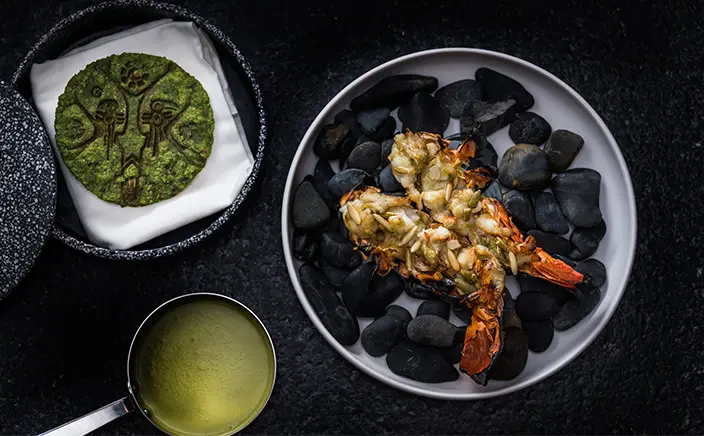 Grilled Caribbean lobster served on hot stones with traditional sauces at Hotel Xcaret Arte, featuring upscale Mexican gastronomy and signature all-inclusive fine dining in Riviera Maya.