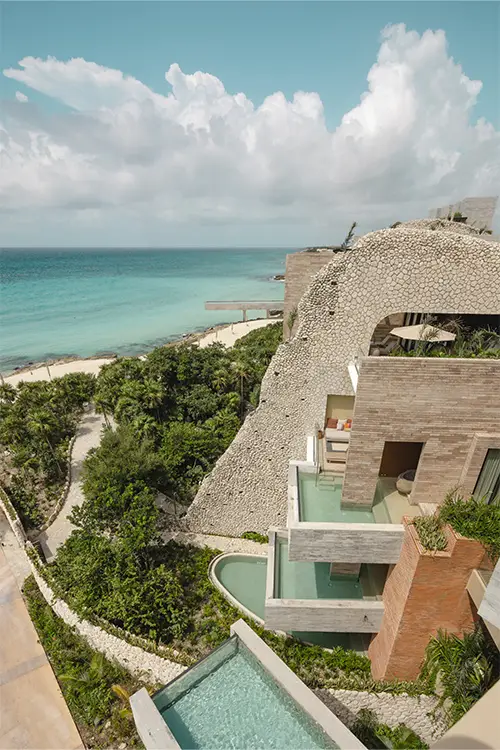 La Casa de la Playa architectural exterior with cascading private pools built into natural stone cliffs overlooking the Caribbean Sea, showcasing ultra-luxury design and intimate boutique resort atmosphere.