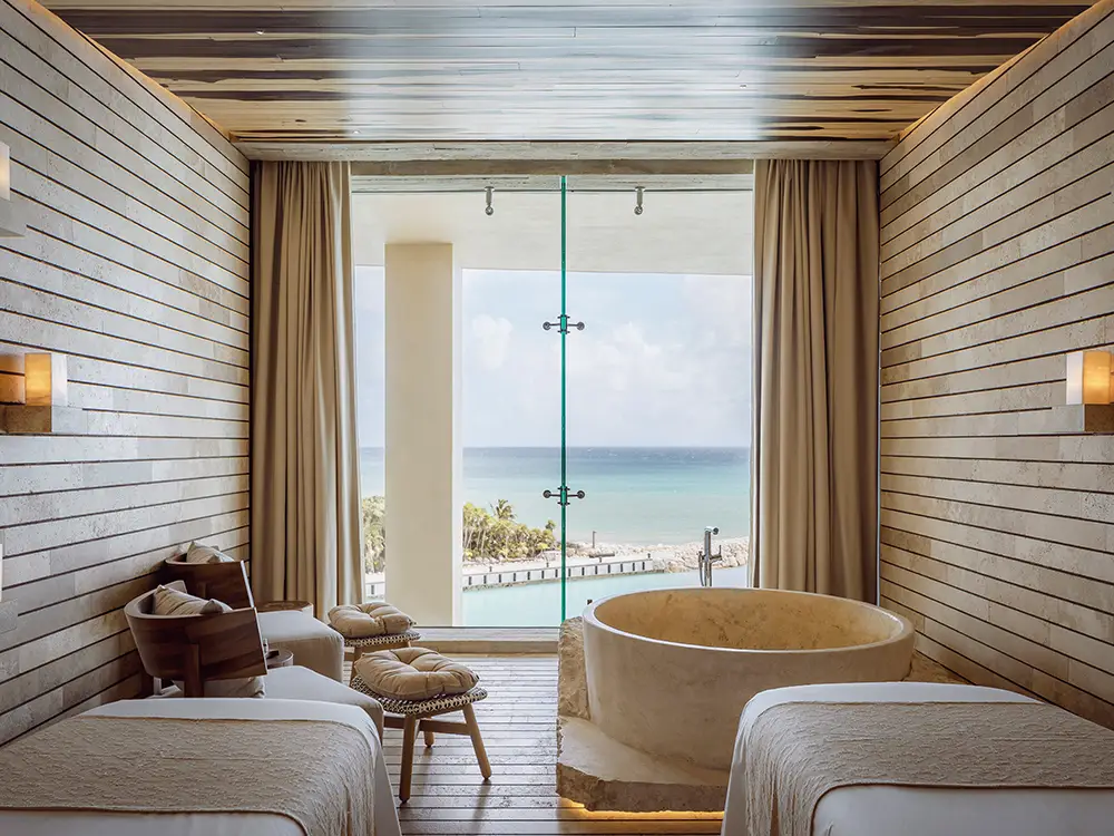 La Casa de la Playa oceanview spa suite with twin massage beds, sculptural soaking tub, and floor-to-ceiling Caribbean views, showcasing ultra-luxury adults-only wellness and personalized Riviera Maya resort experience.