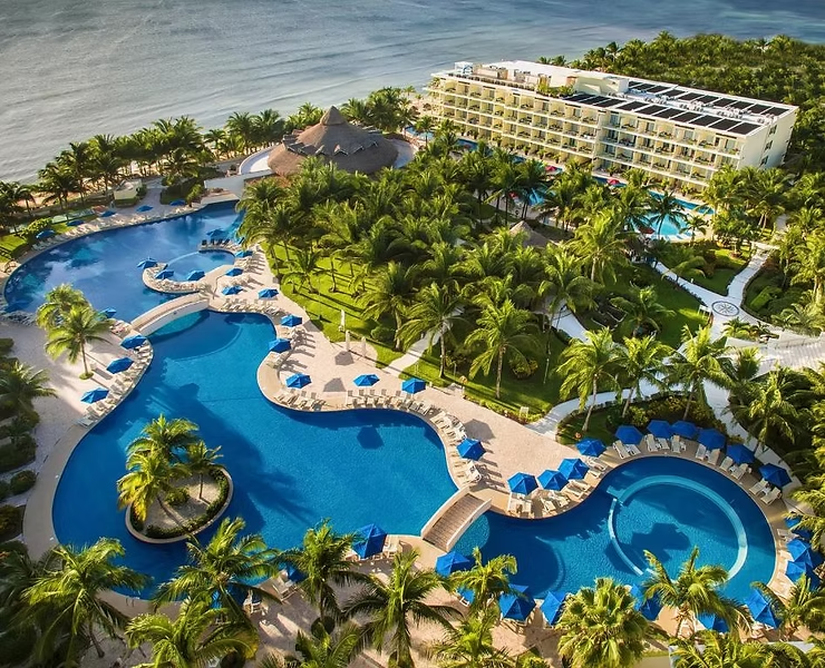 Aerial view of a tropical all-inclusive resort featuring expansive lagoon-style swimming pools, palm-lined pathways, oceanfront accommodations, and beachfront access, highlighting a luxury Caribbean-style resort getaway ideal for relaxation and vacation stays.