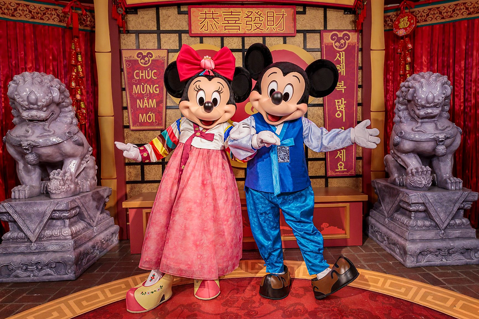 Mickey Mouse and Minnie Mouse dressed in traditional Lunar New Year attire at Disneyland Resort, posing in a festive meet-and-greet location decorated with red lanterns, stone guardian lions, and celebratory signage during the Disneyland Lunar New Year Festival.