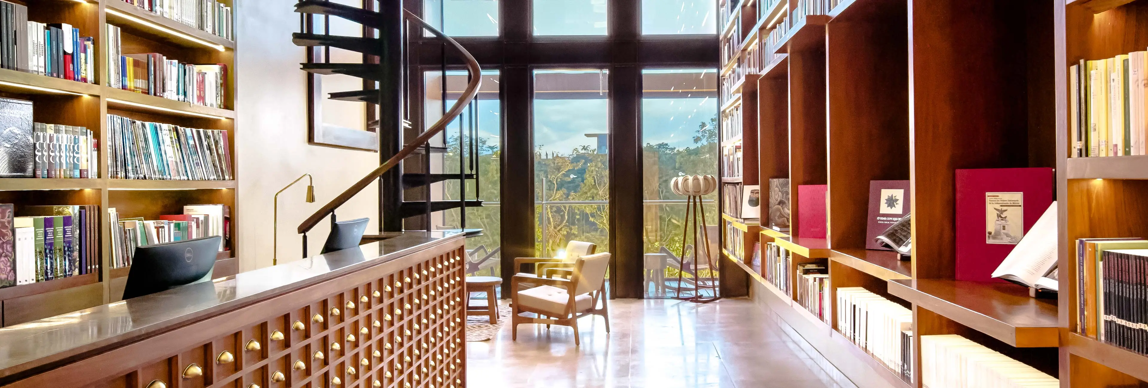 Library and reading lounge with spiral staircase and floor-to-ceiling windows at Hotel Xcaret Arte, showcasing Casa del Diseño-inspired spaces, art-focused amenities, and adults-only Riviera Maya luxury resort experience.