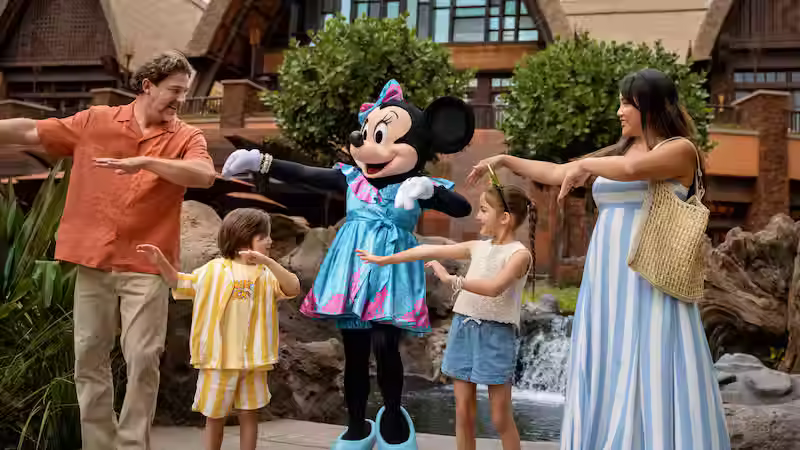 Minnie Mouse dancing with a family near the waterfalls at Aulani, A Disney Resort and Spa, highlighting immersive Disney character meet-and-greets available during limited-time March 2026 Aulani vacation savings with expert planning by Brandi Parker.