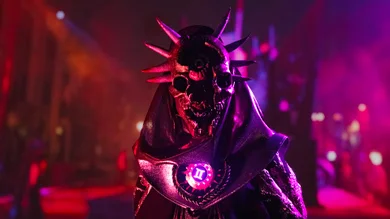 Halloween Horror Nights scare actor wearing a spiked skull mask and glowing chest piece in a dark, neon-lit scare zone.