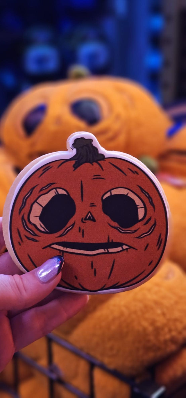 Halloween Horror Nights pumpkin-shaped dessert cookie with spooky face design held in hand, themed seasonal treat at Universal Orlando.