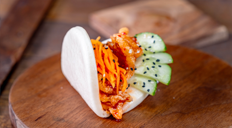 Lunar New Year bao-style taco at Disneyland Resort filled with crispy glazed chicken, pickled carrots, and cucumbers, highlighting a savory seasonal Sip and Savor food offering during the Disneyland Lunar New Year celebration